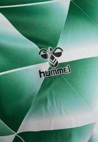Grön och vit mönstrad träningsskjorta i ett mjukt tyg, med Hummel-logotypen i mitten. Designen inkluderar geometriska former.