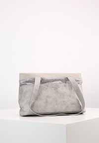Borsa tote in pelle grigia e beige con manici a spalla, forma rettangolare e superficie texturizzata, posizionata su un piedistallo bianco su uno sfondo uniforme.