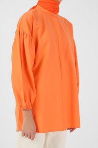Blusa leggera e di un vivace arancione, con maniche a sbuffo, colletto con bottoni e vestibilità comoda. Texture liscia, design minimalista, colore uniforme.