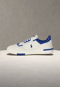 Baskets en cuir blanc avec des accents bleus, des lacets blancs et un logo de cheval brodé en bleu sur le côté, présentées sur un fond neutre.