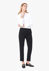 Vit skjorta med spetsig krage, som är kombinerad med svarta slim-fit byxor och svarta loafers med en detalj av guldkedja.