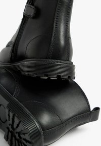 Schwarze Lederstiefeletten mit glatter Oberfläche, ausgestattet mit einem seitlichen Reißverschluss, geriffelter Sohle und verstärkten Nähten für zusätzliche Haltbarkeit.