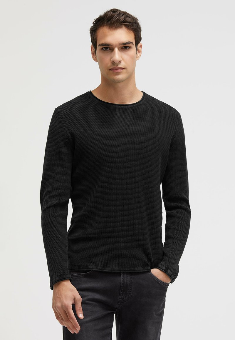 Black long-sleeve shirt with a textured fabric and round neckline, paired with dark jeans. The shirt features a subtle ribbed pattern.