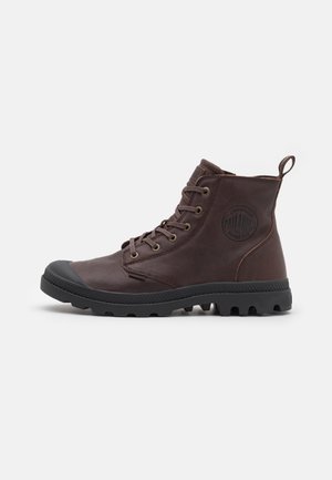 Brown leather ankle boots with black rubber soles, lace-up design, rounded toe, logo patch on the side, and reinforced toe cap.