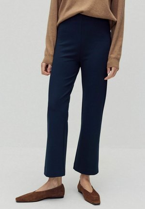 Marinblå vida byxor med slät yta och hög midja, kombinerade med bruna mockaskor. Tyget verkar vara andningsbart och flexibelt.
