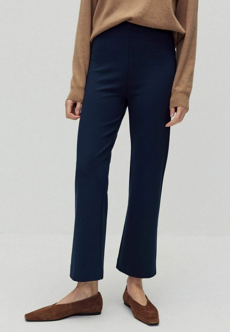 Marineblauwe wijde broek met een gladde structuur en hoge tailleband, te combineren met bruine suède flats. De stof lijkt ademend en flexibel.