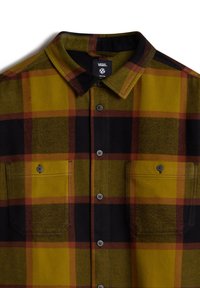 Camicia in flanella a quadri con colori giallo, nero e arancione. Presenta un colletto con bottoni, due tasche sul petto e bottoni grigi. Tessuto morbido.