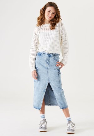 Lichte, witte gebreide trui met een losse pasvorm en open structuur, gecombineerd met een lichtblauwe denim midi-rok met een split aan de voorkant en zakken.