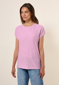 T-shirt rose clair à manches courtes avec un col rond et un motif en vagues texturé à l'avant, assortie à un jean en denim bleu.
