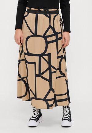 Beige maxiskjørt med svarte geometriske mønstre, elastisk midjebånd og åpninger i sidene, kombinert med svarte høye joggesko med hvite såler.