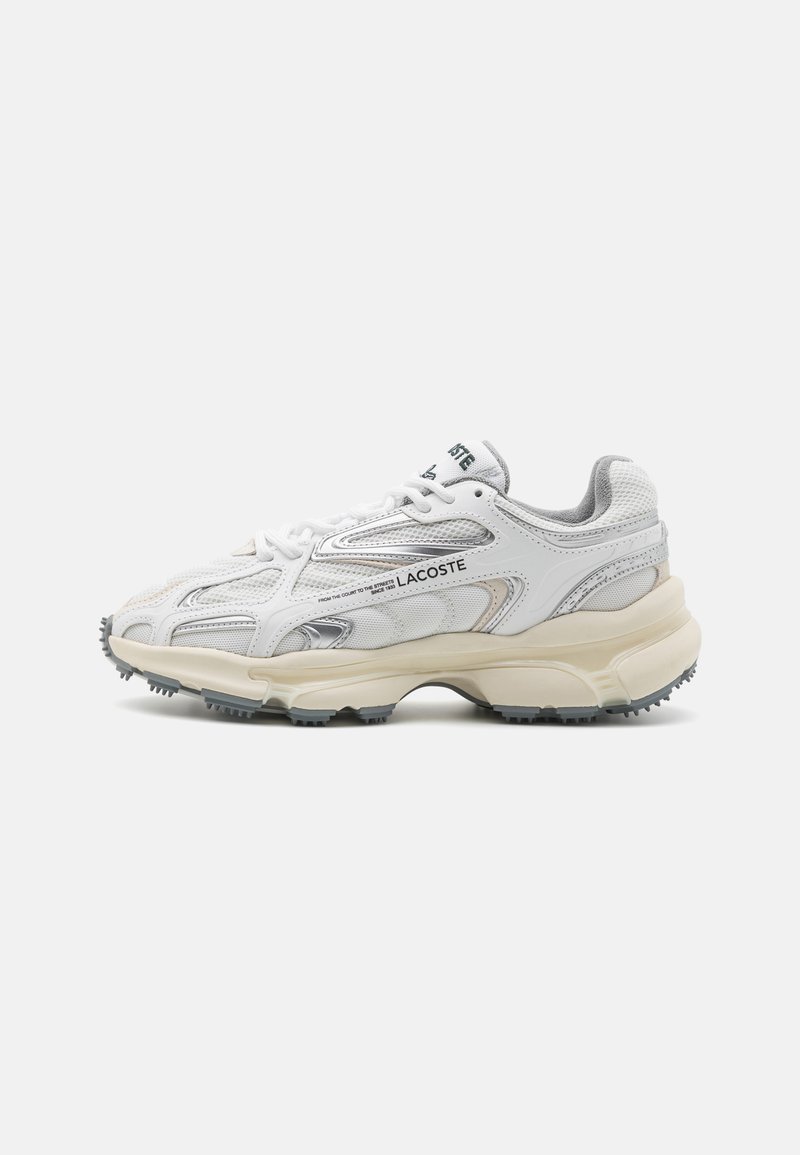 Chaussure de sport blanche Lacoste avec tige en mesh et synthétique, accents argentés, semelle épaisse et semelle en caoutchouc gris texturé pour plus de traction.