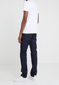 T-shirt blanc à manches courtes, jean bleu foncé et baskets blanches. La tenue présente un design simple et une texture de tissu lisse.