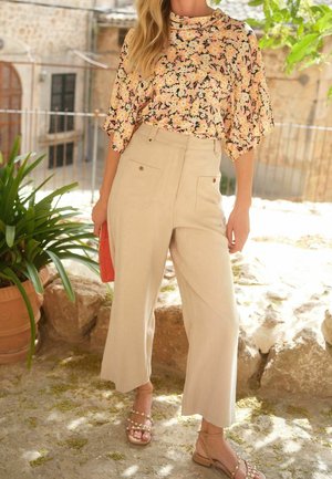 Blumige kurzärmlige Bluse mit einem schwarzen und pastellfarbenen Muster, kombiniert mit hochtaillierten beigen Hosen mit seitlichen Taschen und weitem Bein.