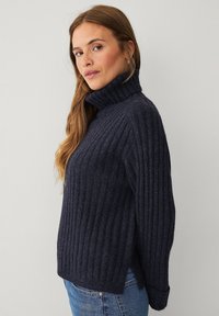Navy ribbed knit turtleneck sweater with long sleeves, relaxed fit, and side slits. Made from soft material for warmth and comfort.