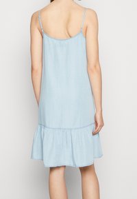 Světle modré denimové šaty s tenkými ramínky, nařaseným pasem a rozšířeným spodním lemem. Hladká textura a jednoduchý, neformální design.