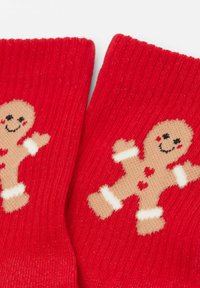 Calze rosse con texture a costine, decorate con un design di un omino di pan di zenzero beige, sorridente, con cuori rossi e risvolti bianchi.