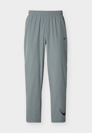 Pantalon de sport gris clair avec une taille élastique, des jambes fuselées et des logos Nike swoosh noirs sur la cuisse supérieure et le bas de la jambe gauche.