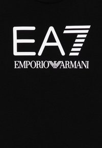 Crna pamučna majica s podebljanim bijelim tekstom: "EA7 EMPORIO ARMANI" s stiliziranim i naglašenim prugama u slovu "7."