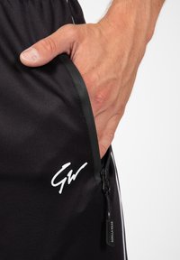 Zwarte shorts met een zijzak met ritssluiting, voorzien van een wit logo en een contrasterende streep. Gemaakt van gladde stof met een matte afwerking.