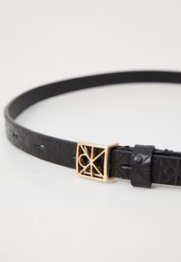 Cintura in pelle nera con motivo geometrico in rilievo, dotata di una fibbia rettangolare dorata con design del logo ritagliato.