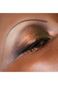 Gros plan sur un œil avec un fard à paupières bronze métallique et vert, un eyeliner bien défini et des cils fournis sur un teint chaud marron.