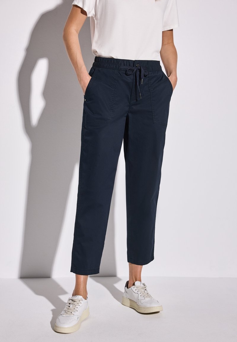 Granatowe spodnie dresowe z elastycznym pasem, sznurkiem, bocznymi kieszeniami i zwężanymi nogawkami. Noszone z białymi trampkami.