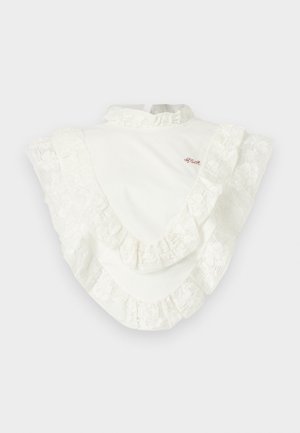 Blouse blanche à col montant avec un large volant en dentelle le long des épaules et de la poitrine, ornée d'un petit texte brodé en rouge sur la partie supérieure de la poitrine.