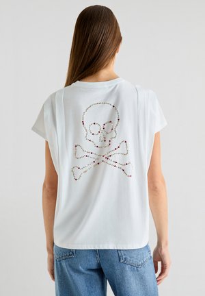 Hvid t-shirt med korte ærmer, der har et skulder- og korsdesign udsmykket med farverige rhinsten på ryggen.