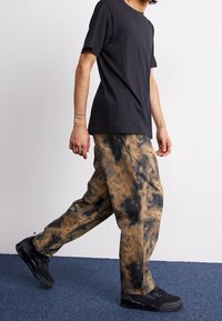 Svart t-shirt med kort ärm i kombination med beige och svart tie-dye byxor. Modellen har på sig svarta sneakers. Avslappnad, lös passform.