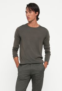 Dark green, long-sleeve crewneck knit sweater with ribbed cuffs and shoulder accent details, paired with gray textured trousers.