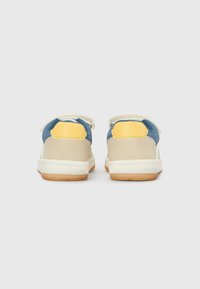 Zapatillas en azul, amarillo y beige con una textura suave. Cuentan con correas ajustables y suelas de goma con dibujo para tracción.