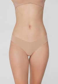 Bezszwowe, cieliste stringi wykonane z miękkiego, lekkiego materiału o gładkim, matowym wykończeniu, charakteryzujące się minimalistycznym designem i brakiem widocznych linii.