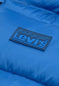 Blå polstret jakke med gummilogo fra Levi's. Har en glatt tekstur og kviltet design for isolasjon og varme.
