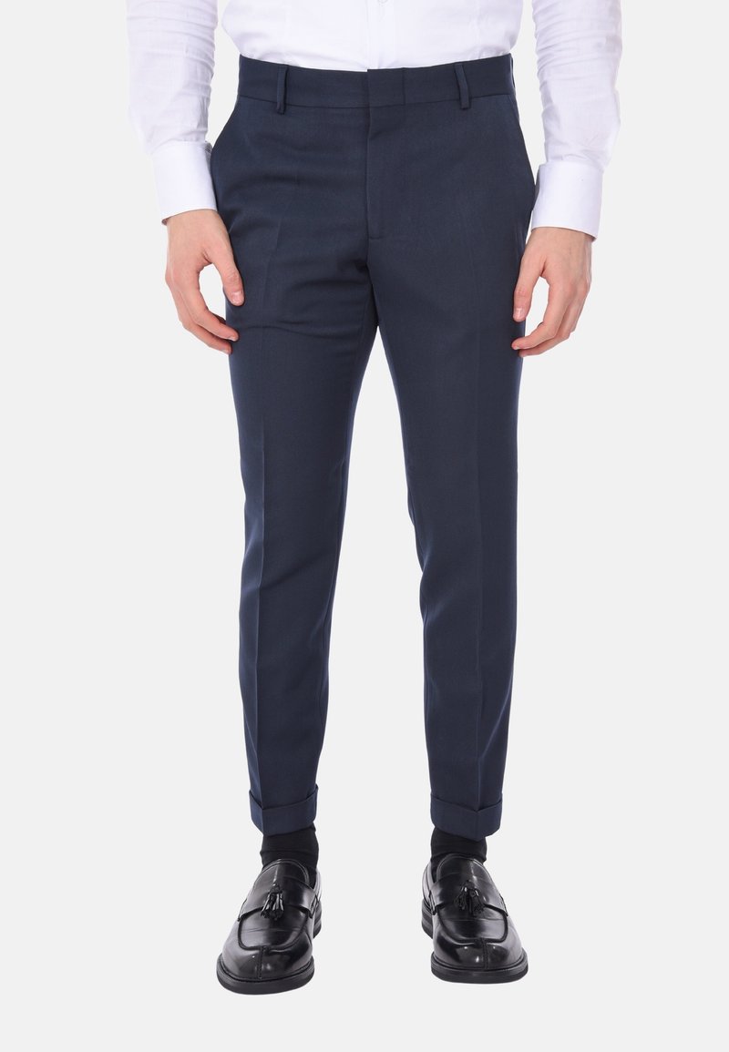 Pantaloni da abito navy realizzati in tessuto liscio, con una vestibilità su misura, tasche laterali e orli risvoltati, abbinati a scarpe nere.