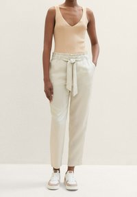 Beige randig linne, ljuskrämfärgade tapered byxor med elastisk midja och knytdetalj, parat med vita sneakers med beige accenter.