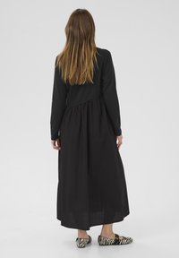 Fekete, hosszú ujjú ruha, gyűrött derékkal, lebegő szoknyával, és lapos cipőkkel, amelyek fekete-fehér zebra mintázatúak. Zökkenőmentes textúra.