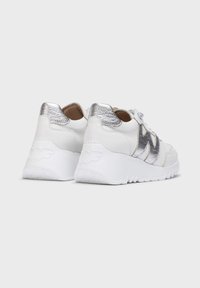 Zapatillas de cuero blanco con un acento metálico plateado en el talón y el logo. Suela blanca gruesa con un patrón texturizado para mayor agarre.