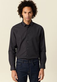 Camicia nera con bottoni e maniche lunghe, colletto e patta frontale. Tessuto morbido con una sottile texture; abbinata a jeans in denim blu scuro.