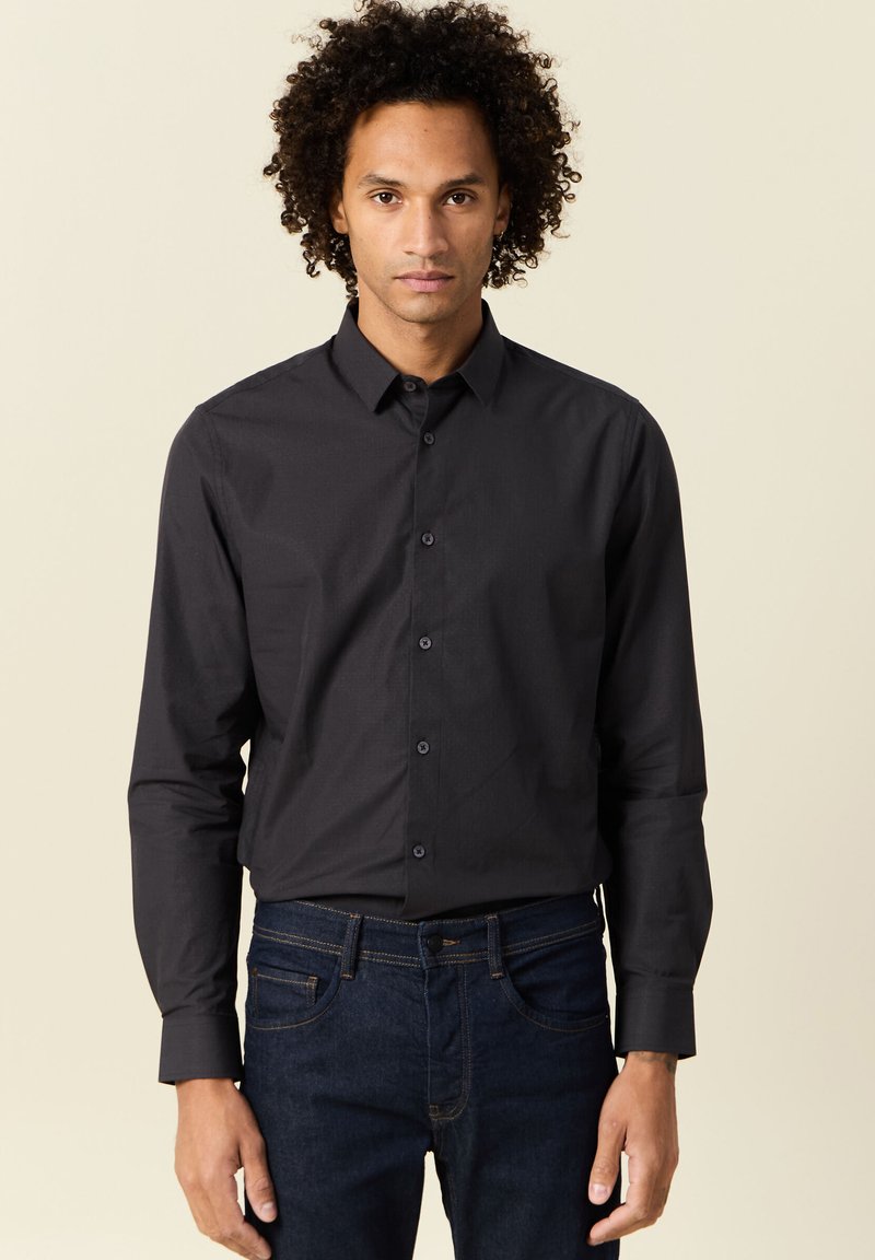 Camicia nera con bottoni e maniche lunghe, colletto e patta frontale. Tessuto morbido con una sottile texture; abbinata a jeans in denim blu scuro.