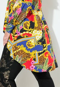 Túnica colorida con estampado floral y detalles de leopardo, hecha de una tela ligera, combinada con leggings negros con acentos dorados.