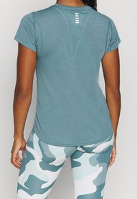 Kortärmad, figursydd atletisk topp i teal med strukturerad tyg och en reflekterande remsa på ryggen. Matchad med ljusblå kamouflageleggings.