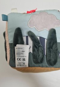 Soft, plush pillow featuring a cloud and trees design with green, blue, and beige colors. Includes care label on one side.