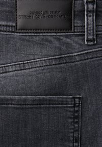 Jeans in denim scuro con tessuto strutturato, etichetta in pelle con testo in rilievo e cuciture a contrasto vicino alle tasche.