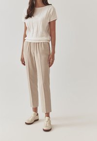 Top bianco a righe con maniche corte abbinato a pantaloni beige su misura. Sneaker neutre completano l'outfit, enfatizzando gli elementi di design contemporaneo.