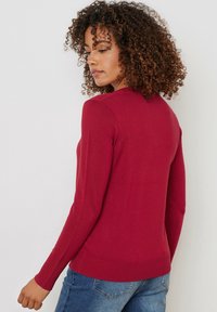 Röd stickad tröja med långa ärmar och rund halsringning. Slim-fit design med ribbade ärmslut och nederkant, som visar en jämn textur.