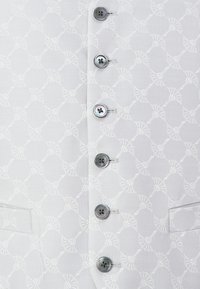 Weißer Stoff mit einem subtilen gewebten Muster aus Knoten, ausgestattet mit sechs Knöpfen in Silber und Schwarz sowie einem seitlichen Taschen-Detail.