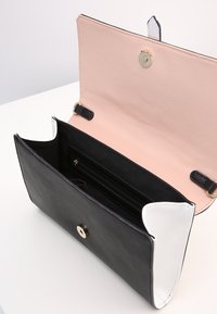 Czarny i biały skórzany portfel z różowym wnętrzem, z zapięciem na zatrzask i wieloma przegródkami, w tym kieszenią zapinaną na zamek.