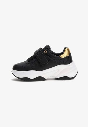 Sneaker nera spessa con suola bianca spessa, cinturino in velcro, loghi in rilievo e accento in oro metallizzato sul tallone.