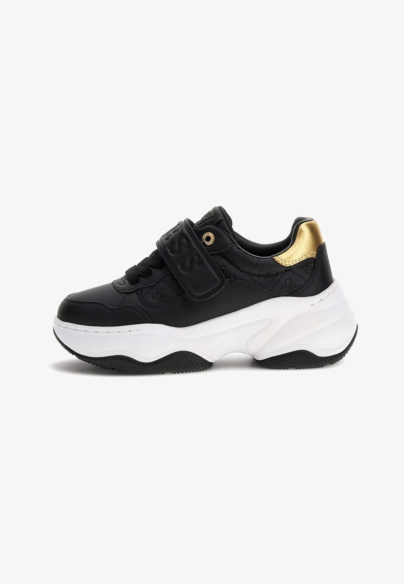 Schwarze klobige Sneaker mit dickem weißen Sohlen, Klettverschluss, geprägten Logos und metallic-goldenem Fersenakzent.