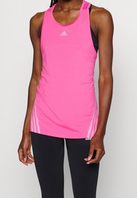 Vaaleanpunainen urheilullinen toppi, jossa on pyöreä kaula-aukko, hienovarainen logo ja kolme raitaa sivuilla, valmistettu sileästä ja kevyestä kankaasta.